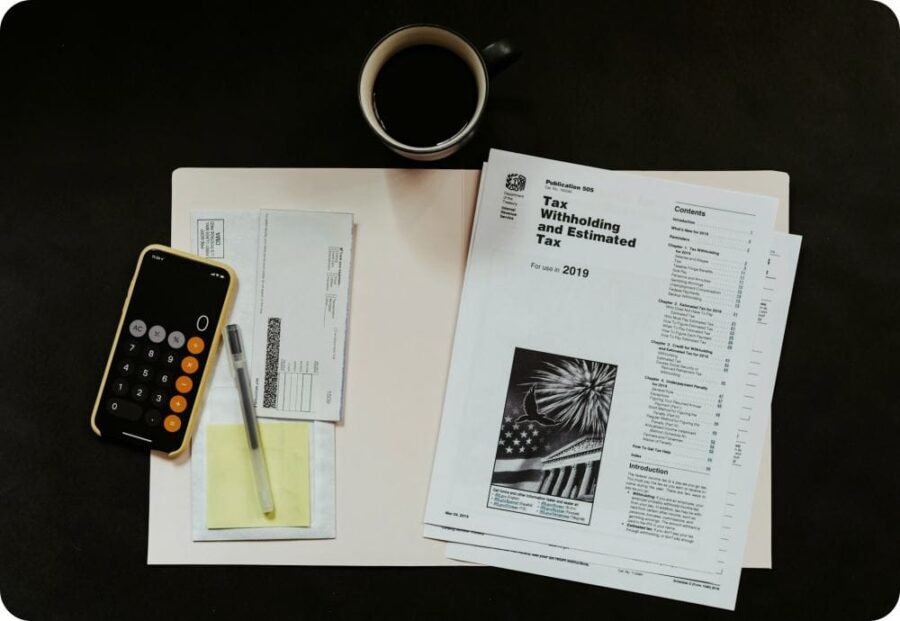 Black and white tax documents in a file and a calculator and pen next to them