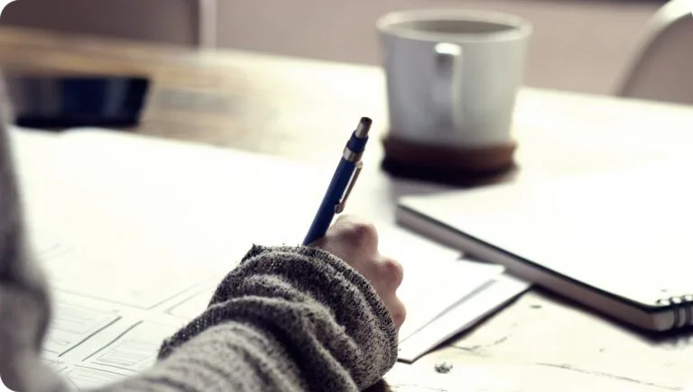 a person studying on a brown wooden table near a white mug
